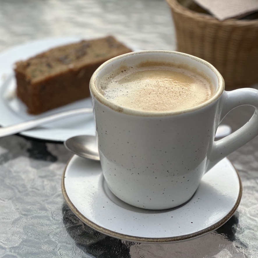 Una taza de café sobre su plato, con una rebanada de pan al fondo